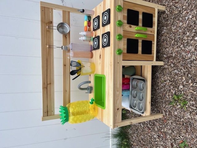 Outdoor mud kitchen stocked with pots, pans, and utensils