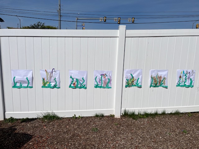 Children's underwater seaweed paintings displayed along the outdoor fence