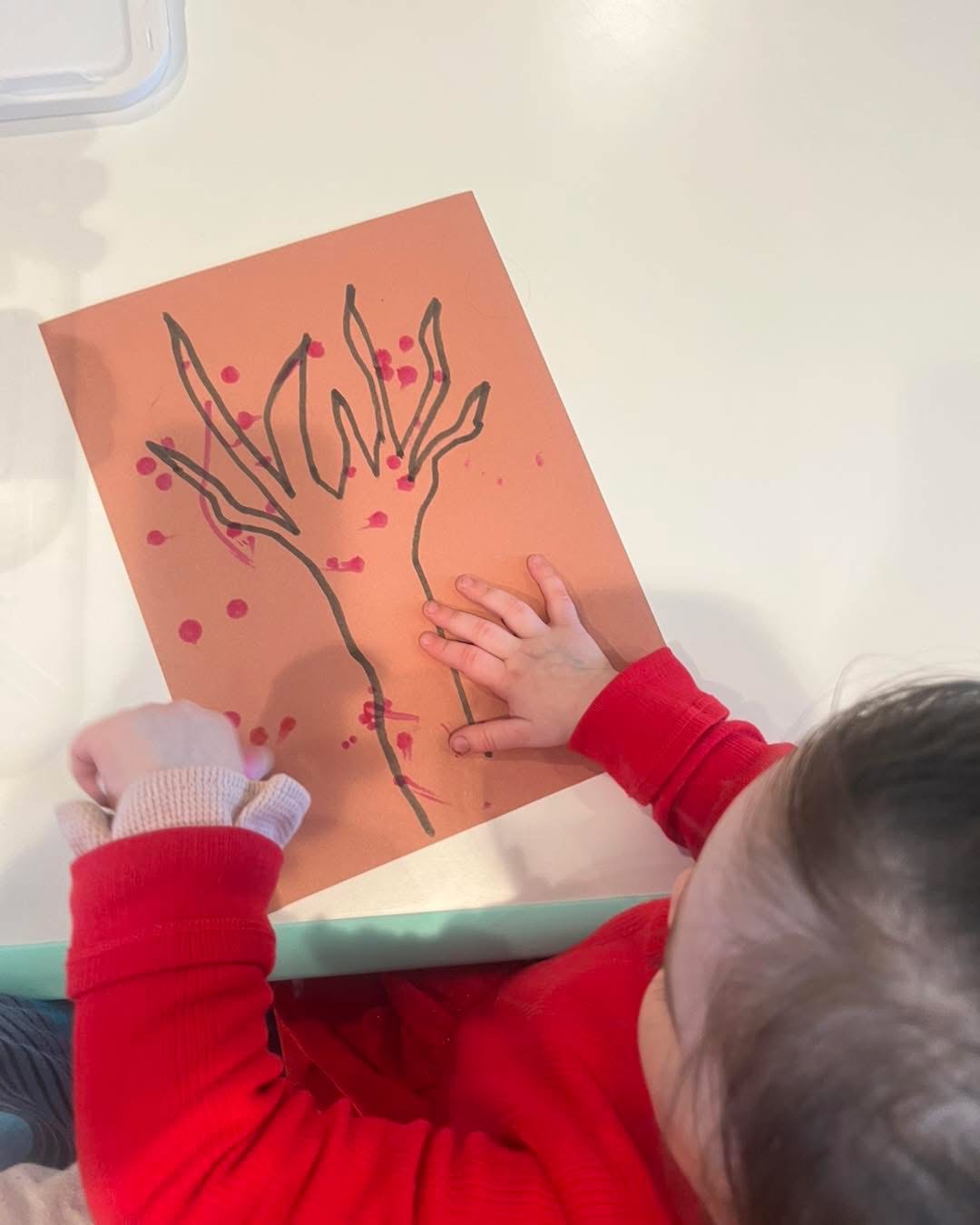 Child painting cherry blossoms on orange paper