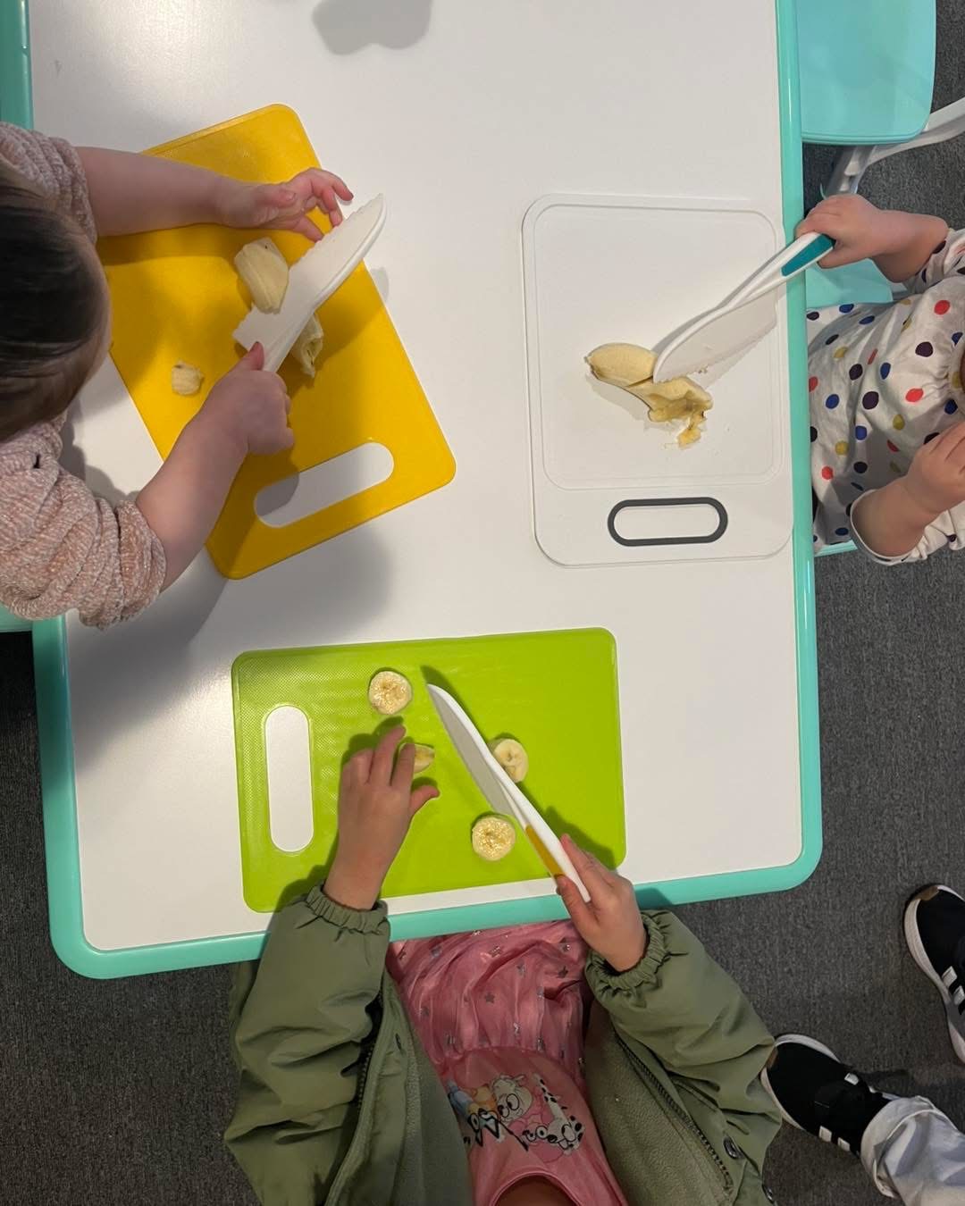 Toddlers slicing bananas with safe knives at the table