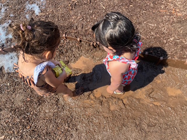Friends splashing and digging in a mud puddle outside