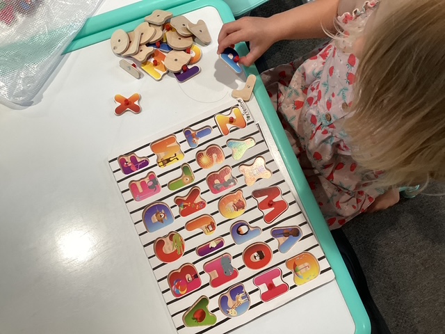 Working on a wooden alphabet puzzle at the table