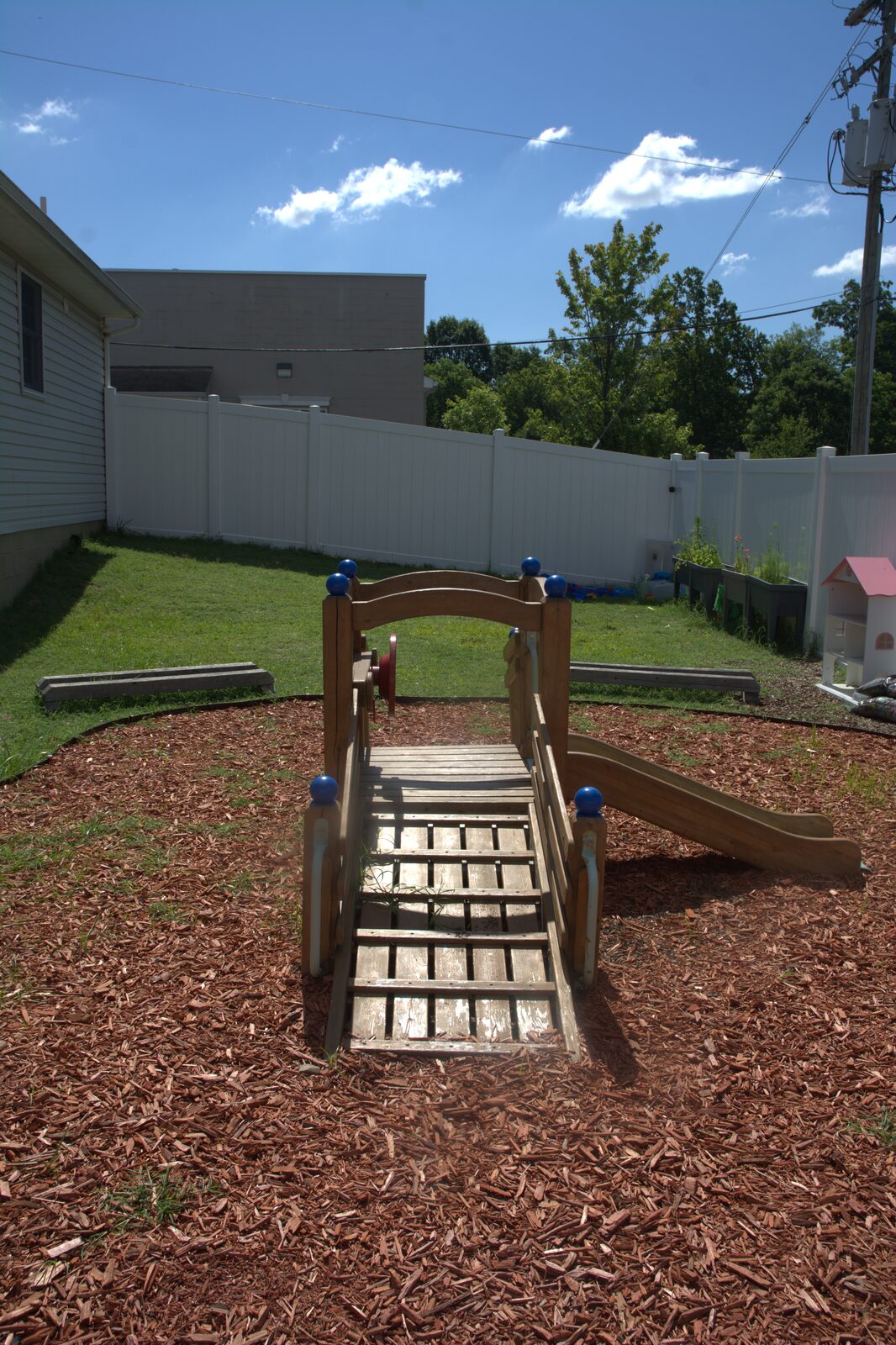Fenced backyard play area with a wooden bridge climber